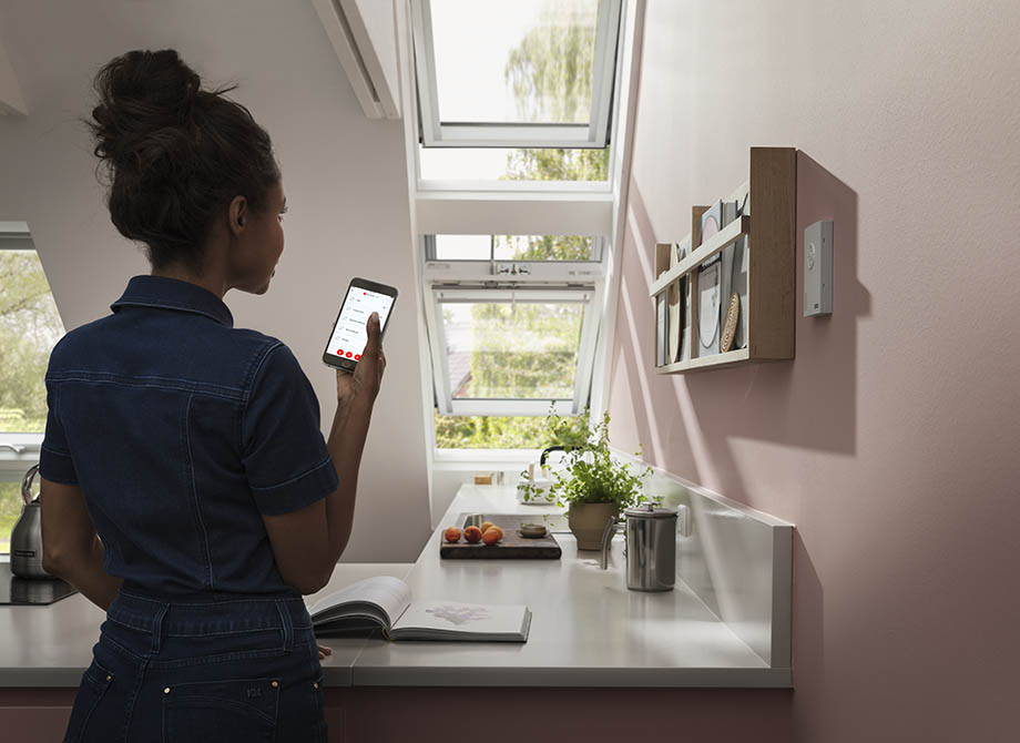 Woman controlling her VELUX roof windows with the VELUX ACTIVE app on her smartphone.